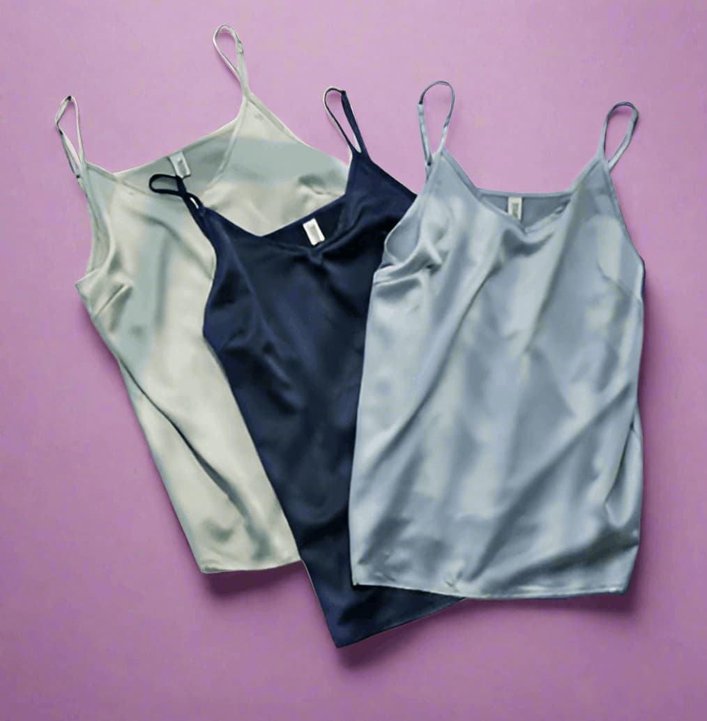 Three satin slip dresses in silver, navy, and gray on a purple background