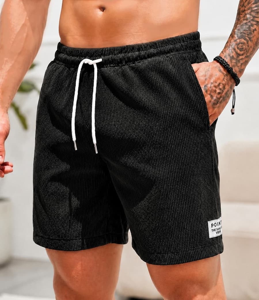 Black textured corduroy shorts with a white drawstring and a small white patch on the lower left leg, shown on a model.
