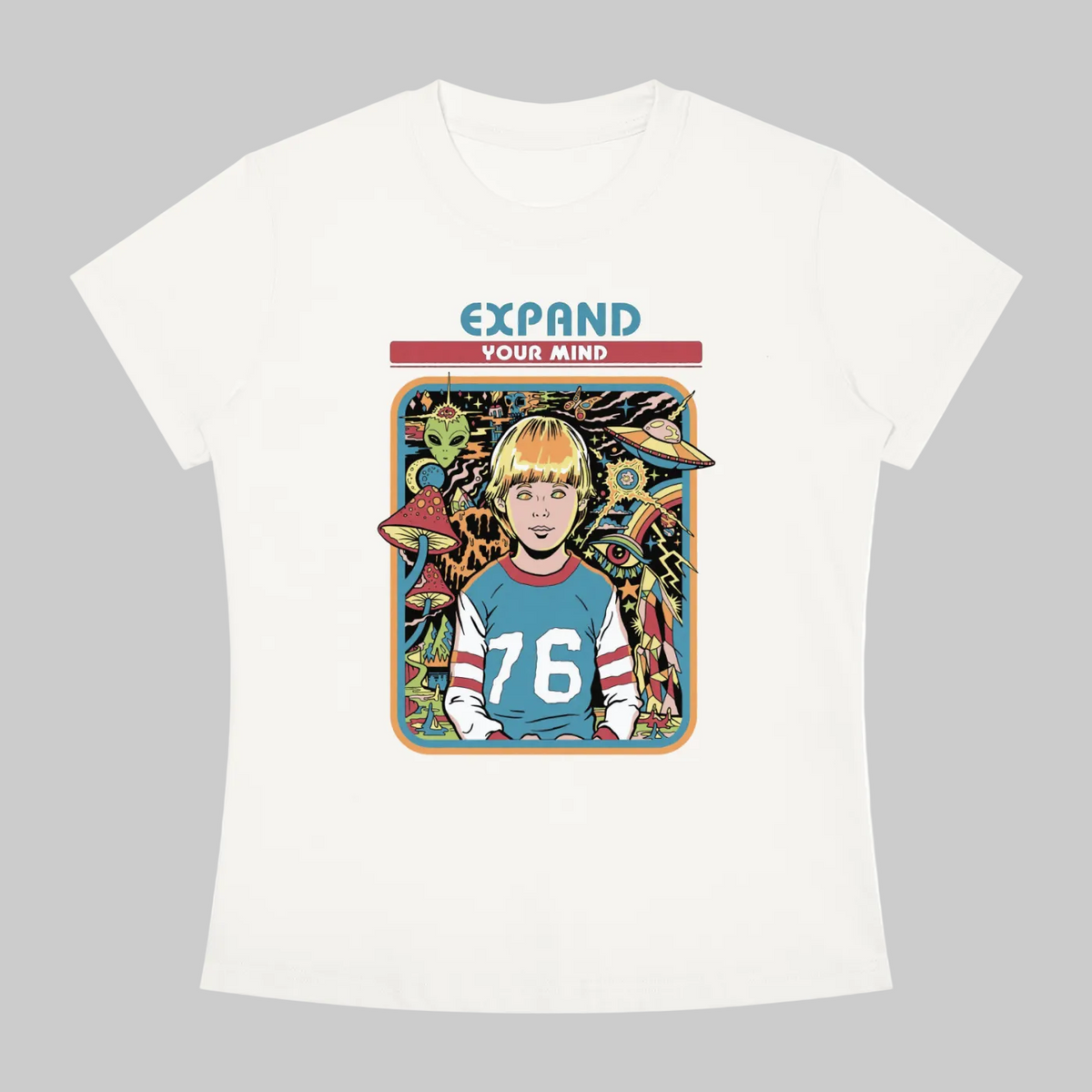 An off-white short-sleeve crewneck t-shirt featuring a colorful graphic print on the front. The graphic shows a cartoon-style portrait of a blonde boy wearing a blue jersey with the number 76, surrounded by retro sci-fi elements like a UFO and alien, with the text 'EXPAND YOUR MIND' above.