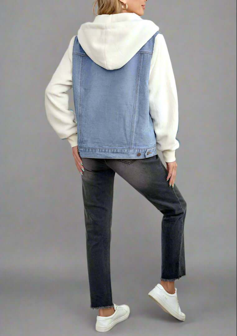 Woman wearing a denim vest over a white hoodie in a bedroom setting