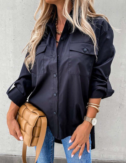 Person wearing a black button-up shirt and blue jeans, holding a tan handbag against a gray background