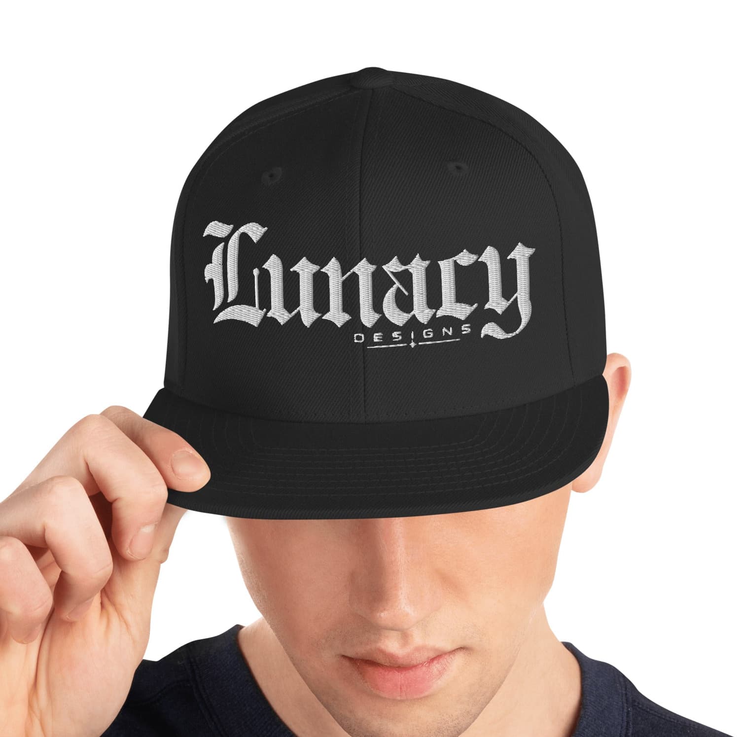 A man wearing a black snapback cap with 'Lunacy Designs' embroidered in white Gothic lettering on the front, holding the brim with his hand against a plain white background.