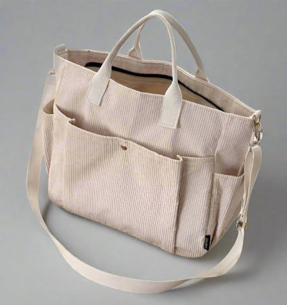 Beige tote bag with multiple pockets and straps on a gray background