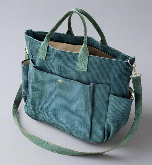 Teal tote bag with multiple pockets and a shoulder strap on a light gray background
