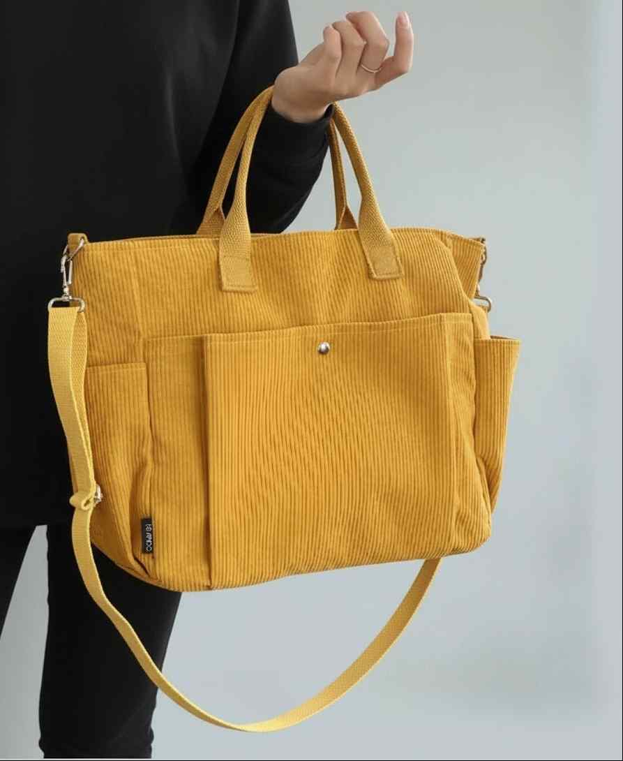 Yellow corduroy bag held by a person against a light gray background