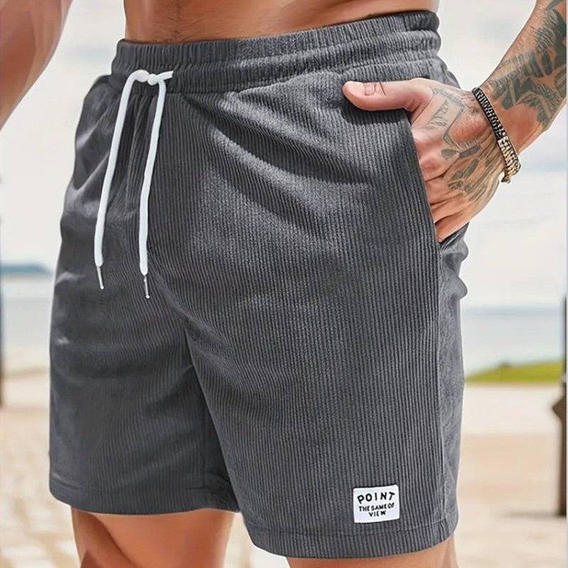 A man stands with one hand in a pocket, displaying men's corduroy shorts in grey
