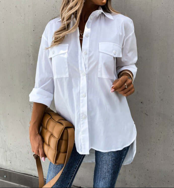 A woman wearing a white shirt is standing against a gray wall.